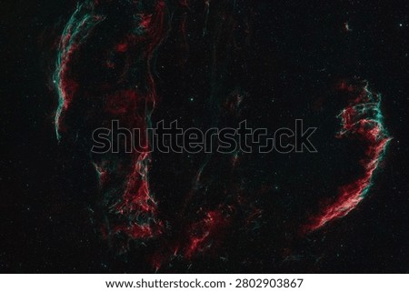 A deep space image shows the red and green gas filaments of a nebula against a dark background of stars.