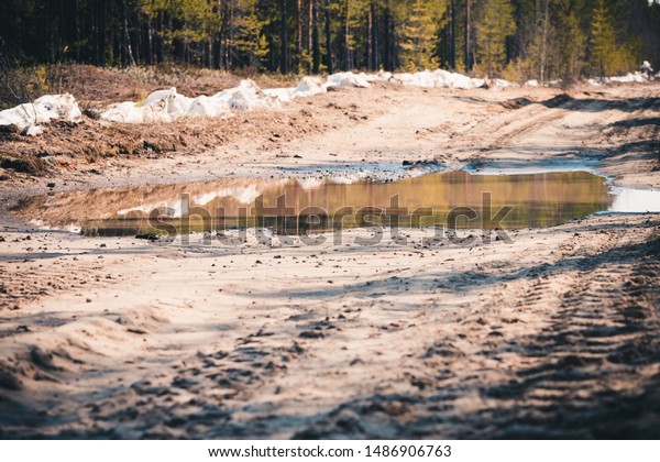 Deep spring puddle on the sandy road due to\
melting snow after winter