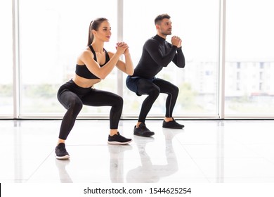 Deep squat. Fitness couple in sportswear doing squat exercises at gym, copy space