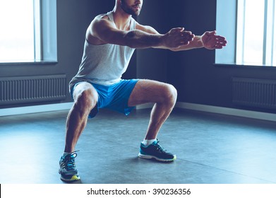 Deep squat. Part of young man in sportswear doing squat at gym