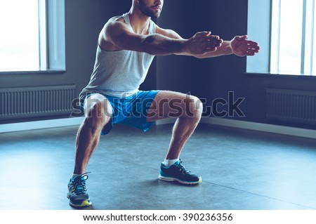 Deep squat. Part of young man in sportswear doing squat at gym