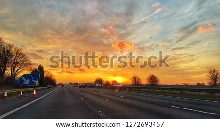 Deep sunrise over the motorway in England.  detailed cloudy sky with deep orange horizon.  taken with a wide angle lens to get the super wide angle image. 