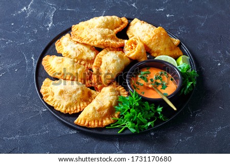 deep-fried Buffalo Chicken Empanadas with Low-Calorie Dip on a black platter on a concrete table, horizontal view from above