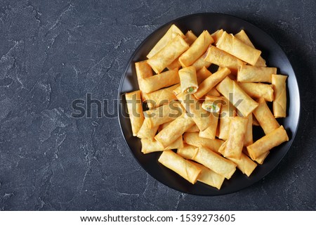 deep-fried crispy chinese spring rolls with cabbage, carrots and green peas fillings on a black plate on a concrete table, view from above, flatlay, free space
