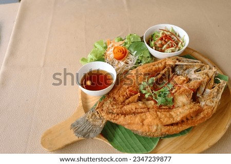 Deep-fried sea bass with fish sauce is popular dish. Deepfried sea bass with fish sauce served with mellow dipping sauce with sliced ​​mango to add flavor and fresh vegetables arranged in wooden plate