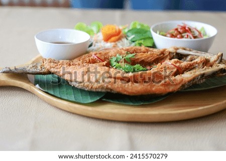 Deepfried sea bass with fish sauce served with mellow dipping sauce with sliced ​​mango to add flavor and fresh vegetables arranged in wooden plate. Deep-fried sea bass with fish sauce is popular dish