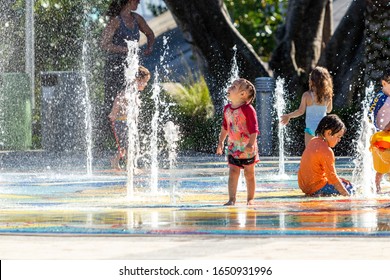 Deerfield Beach, FL / USA - 2/17/2020: Children in bathing suit playing in the splash pad water fountain in the sun at Sullivan Park in Florida with mothers and parental guardians nearby watching.