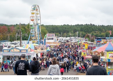 Deerfield, New Hampshire, USA - October 03, 2021: View of crowded fairground with colorful vendor booths and ferris wheel in background at the Deerfield Agriculture Fair in New Hampshire