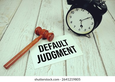 Default Judgment text on paper card with alarm clock and wooden judge gavel top view on wooden background