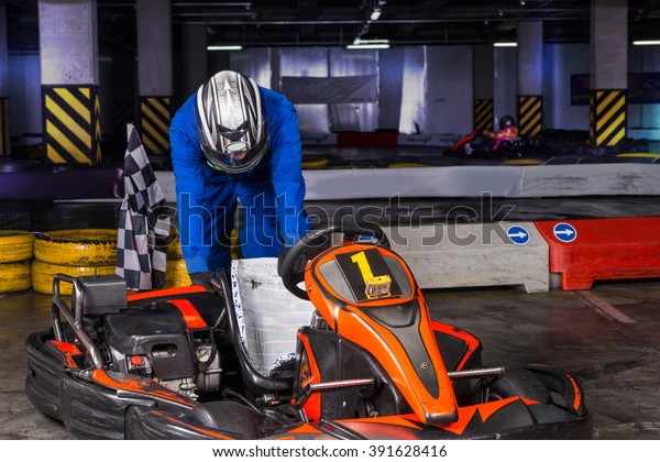 Defeated bumper car driver in helmet and blue\
jumper hangs his head and braces against his ride while parked in\
amusement park\
building