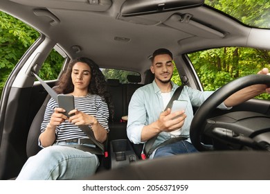 Defensive, Not Safety Driving Concept. Young Arabic Man And Woman Using Smartphones While Travelling By Car Together, Gadget Addicted Millennials Sitting Inside Nice Auto, Checking Social Media