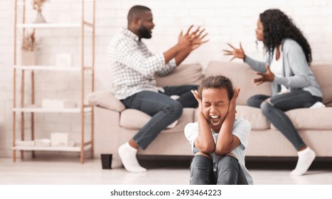 Defensive reaction. Upset little black girl sitting on floor, yelling and closing ears not to listen parents arguing, selective focus on child - Powered by Shutterstock