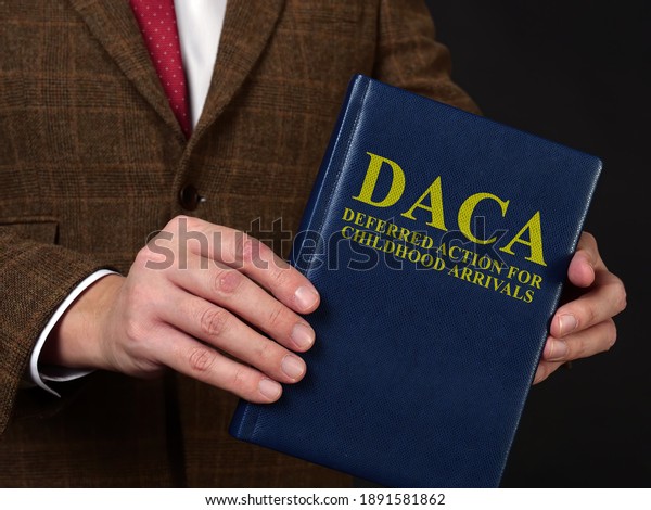 Deferred Action for Childhood Arrivals DACA\
concept. Man in suit shows the\
book.