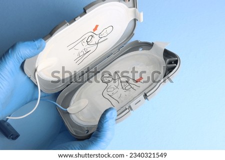 Defibrillator electrodes in the case beeing opened in a light blue background by a professional wearing gloves 