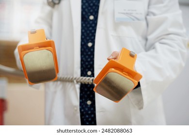 Defibrillator, hands and doctor in hospital with cardiology, electric shock and equipment for cardiac care. Clinic, surgeon and person with emergency gear for support of heartbeat for heart attack - Powered by Shutterstock