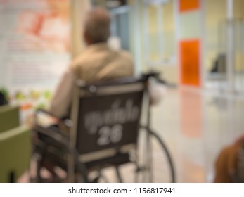 Deficused Image, Elderly Patients Sitting On Wheelchair Waiting For The Doctor In Front Off Emergency Room, At Hospital, With Space For Text.