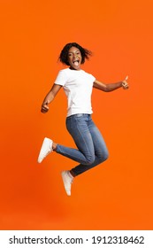 Definitely Recommend It. Emotional Young Black Woman Jumping In The Air And Screaming, Showing Thumbs Up, Happy African American Lady Expressing Positive Emotions On Orange Studio Background