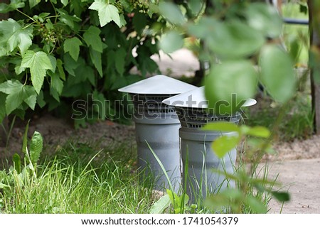 Deflector on a gray ventilation pipe among green leaves