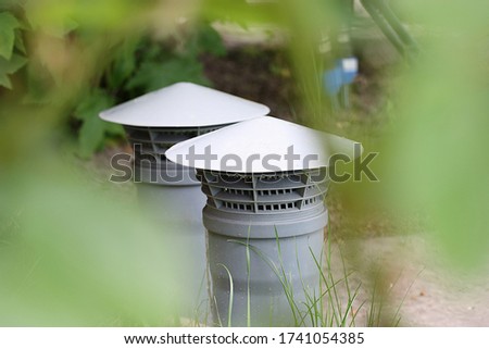 Deflector on a gray ventilation pipe among green leaves