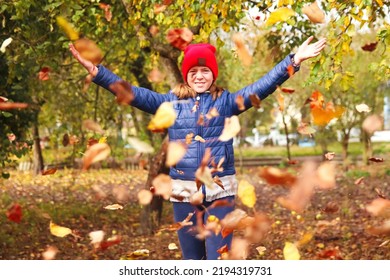 Defocus Autumn People. Teen Girl Raising Hand And Throwing Leaves. Many Flying Orange, Yellow, Green Dry Leaves. Enjoy Autumn. Happy Fall. Funny Season. Smiling Kid. Out Of Focus.