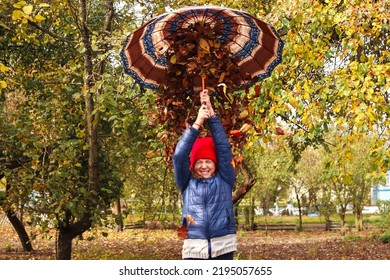 Defocus Autumn People. Teen Girl Holding Umbrella And Throwing Leaves. Many Flying Orange, Yellow, Green Dry Leaves. Enjoy Autumn. Happy Fall. Funny Season. Smiling Kid. Out Of Focus.