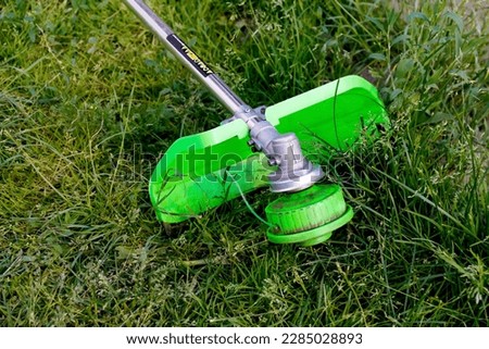 Defocus grass trimmer. A man mowing the grass. Outdoor view of a lawn trimmer mower cutting grass in a blurred nature background. Housework. Cutter edger. Out of focus.