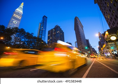 Defocus Motion Blur View Of Yellow Taxis Driving Through The City Streets At Dusk In New York City, USA. Slow Shutter Speed To Enhance Motion Blur Effect.