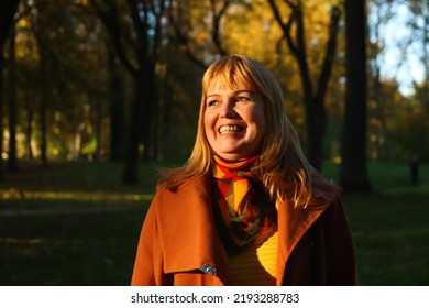 Defocus portrait of middle aged Caucasian blonde woman in autumn park. Bright stylish woman in orange coat and shawl of neck. Happy fall concept. Sunny weather, sunset. Dark shadows. Out of focus. - Powered by Shutterstock