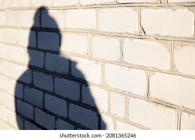 Defocus Shadow Of Person In Winter Cap On White Brick Wall. Light And Shadow Women. Female Person Silhouette. People Shadows With Reflection On The House Wall, Outdoor.