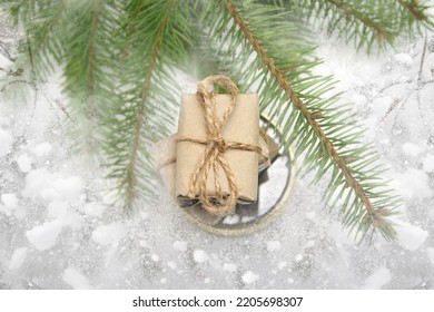 Defocus stack of craft little gifts standing on round gold mirror on snowy background. Christmas holiday concept. Wish list. Retro, antique, vintage. Natural green fir branches. Eco box. Out of focus.