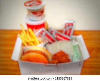 Defocused abstract background of box containing lunch menu. Namely rice, KFC fried chicken, chicken burger, fries, chili sauce, as well as soft drinks and desserts.