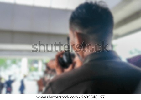 Defocused abstract background close-up of security guard with short haircut holding walkie talkie radio during official outdoor event