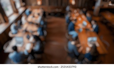 Defocused abstract background in a rustic café with warm earthy tones, showing diverse individuals working on laptops at long wooden tables in a creative space.
