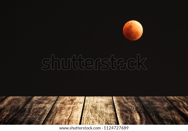 Defocused background of eclipse lunar blood moon
in dark sky with copy space and decorated with clear wooden terrace
or floor / scientific
concept