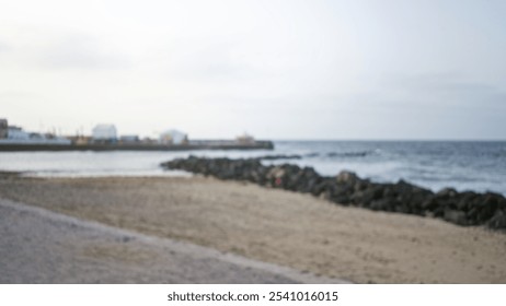 Defocused beach scene in lanzarote, spain with sandy shore, ocean waves, blurred background, rocky outcrop, bokeh effect, and blurred figures in the distance - Powered by Shutterstock