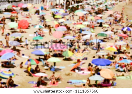 a defocused blur background of a packed beach, with many umbrellas of different colors, in summer
