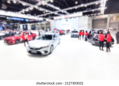 Defocused Blurry Crowd Anonymous People Walking At The Exhibition Car Show At Convention Event Or Conference Hall. Light Bokeh Background. Business Of Car Sales Or Purchases For Customers.