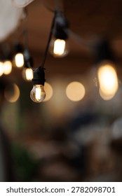 Defocused bokeh string lights with warm Edison bulbs hanging at outdoor evening cafe terrace