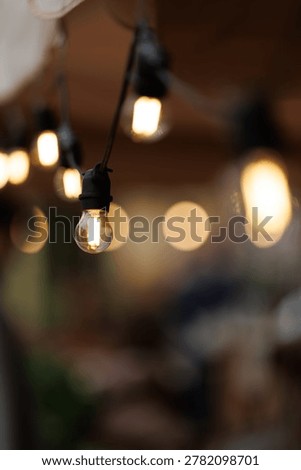 Defocused bokeh string lights with warm Edison bulbs hanging at outdoor evening cafe terrace