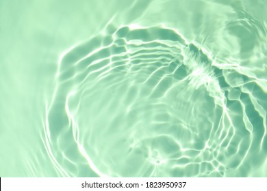 De-focused closeup of mint green transparent clear calm water surface texture with splashes and bubbles. Trendy abstract summer nature background. Mint colored waves in sunlight with copy space.