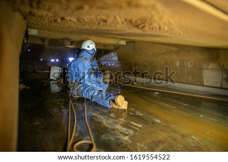 Defocused construction worker wearing safety harness disposable contaminate protective clothing connecting Karabiner which attached harness loop rescue precaution while working in confined spaces