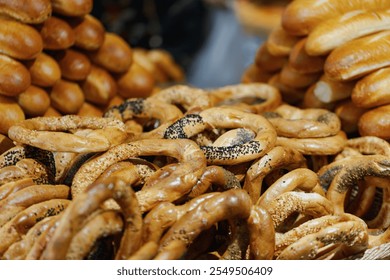 Defocused freshly baked bread rings and rolls are stacked together, showcasing a variety of textures. Golden, crusty loaves with sesame and poppy seeds, emphasizing traditional bakery goods. - Powered by Shutterstock