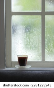 defocused, A glass of black coffee on the Window Sill, with against the warm light from the sunny day outside.