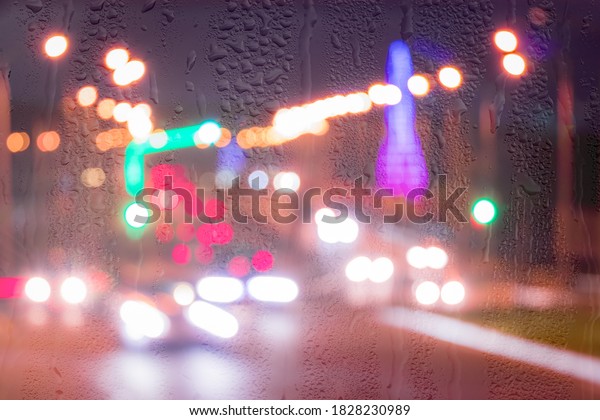Defocused\
headlights from moving cars behind rainy, wet glass at night.\
Abstract concept of rainy autumn\
weather.