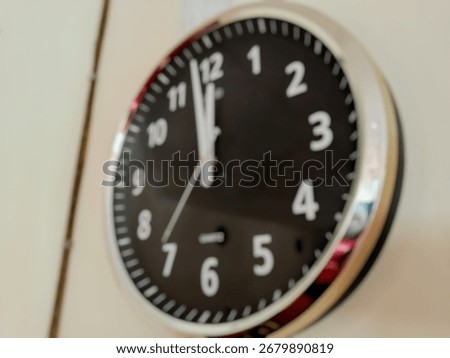 defocused image of a black wall clock showing exactly twelve o’clock, symbolizing punctuality, deadline, and time management