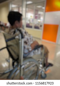 Defocused Image, Elderly Patients Sitting On Wheelchair Waiting For The Doctor In Front Off Emergency Room, At Hospital, With Space For Text, Blur Background. Selective Focus.