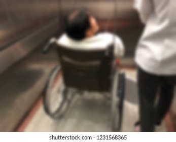 Defocused Image, Elderly Patients Sitting On Wheelchair Waiting For The Doctor In Front Off Emergency Room, At Hospital. Selective Focus.