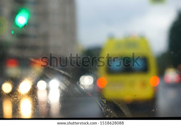 Defocused\
image of emergency ambulance travels through city street seeing\
through the wet from rain wind screen of a\
car.
