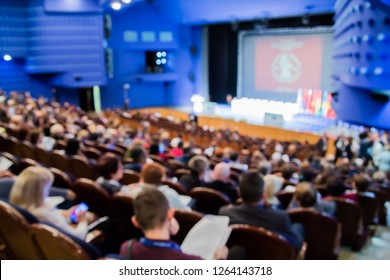 Defocused Image. People In The Auditorium. International Conference. Flags Of Different Countries On Stage.