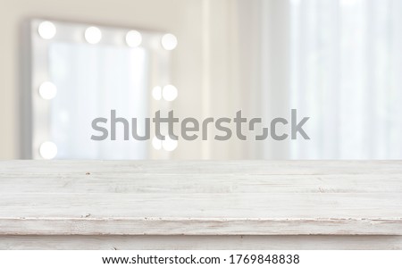 Defocused makeup mirror in dressing room with wooden table top